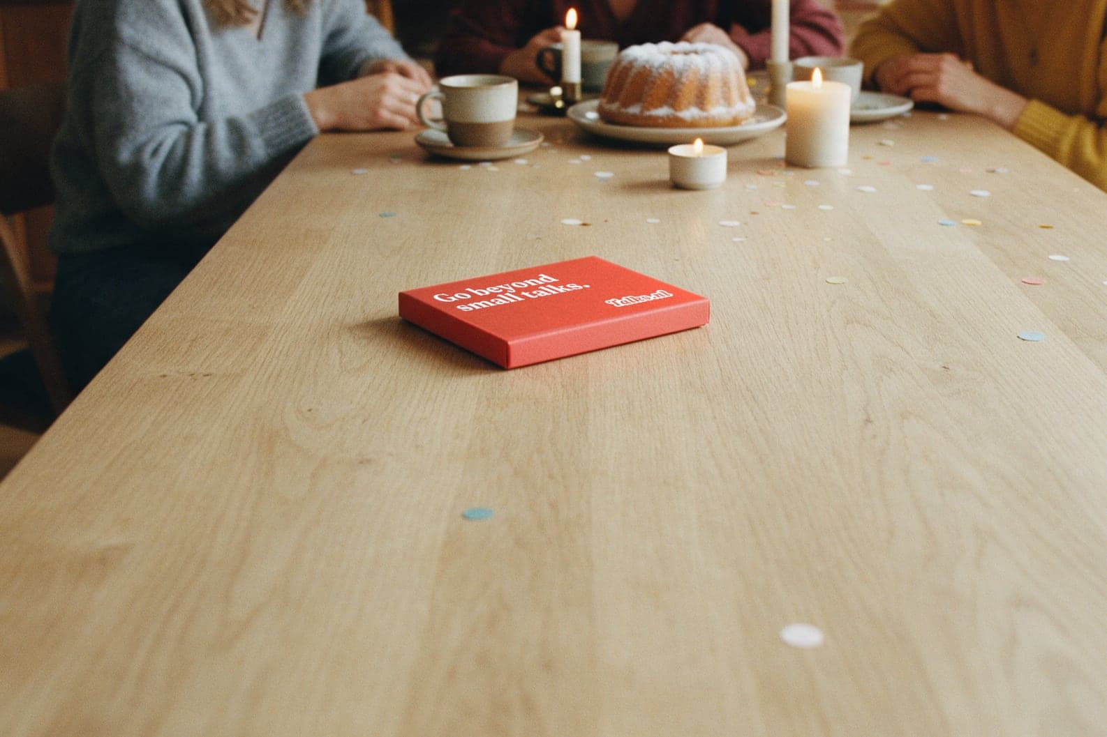 Het vlamrode Talks.nl cadeaudoosje op een eettafel, met daarachter vriendinnen met koffie, taart en kaarsjes